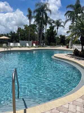 A clear swimming pool with a metal ladder, surrounded by palm trees and lounge chairs. - 
Nature Retreat3/2 Near Disney &Beaches  Peaceful Apartment Surrounded by Nature (Poinciana)