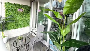 A balcony with a green wall, a chair, a table, and a large plant.