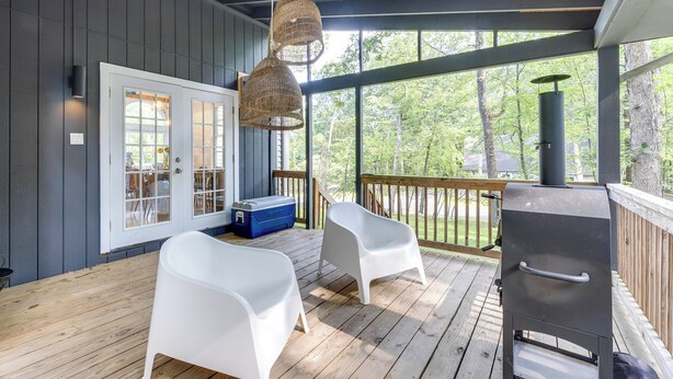 Een overdekt terras met houten vloer, witte plastic stoelen, een barbecue en een blauwe koelbox.