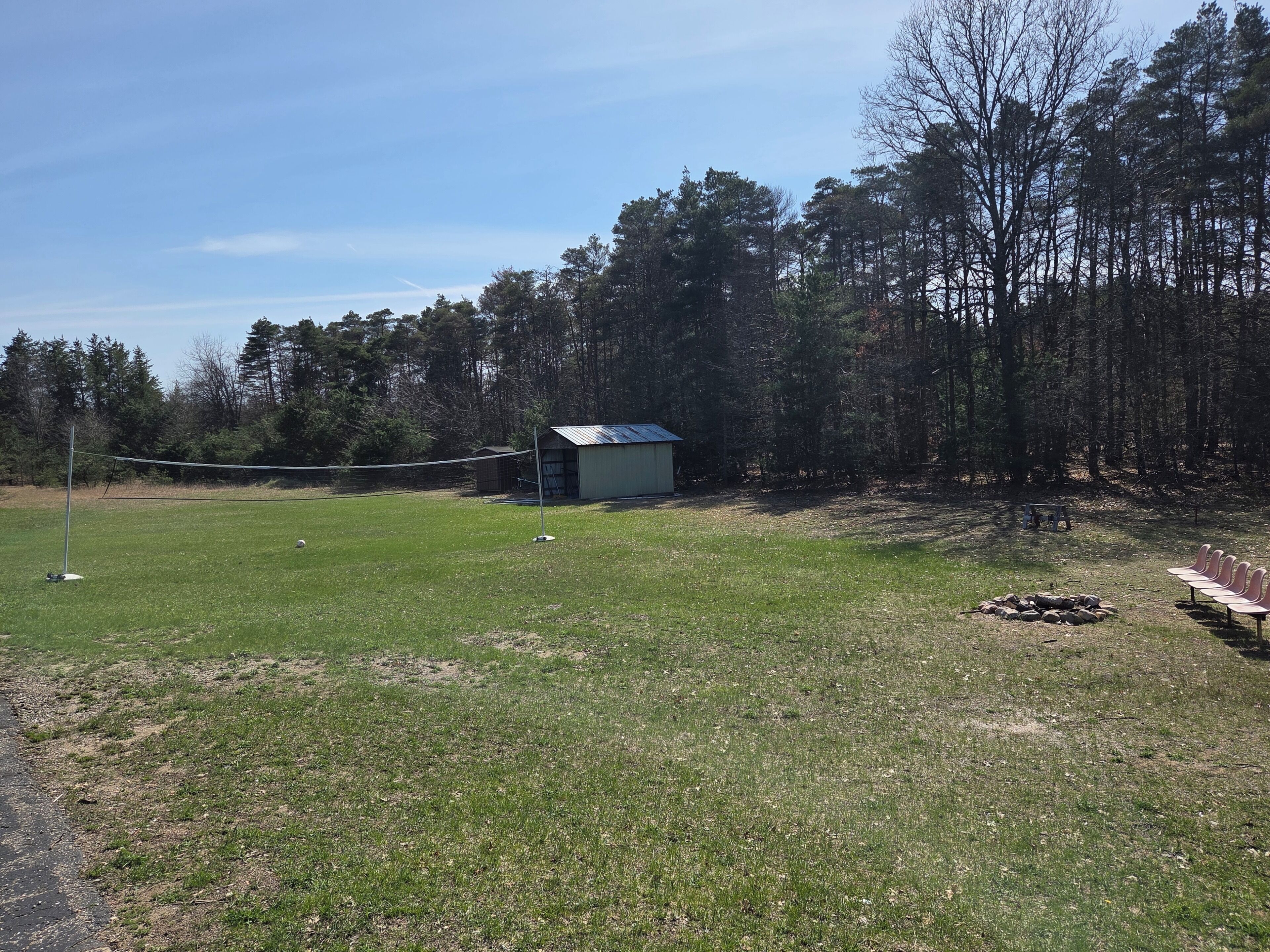 Een grasveld met een klein tuinhuisje, een vuurkorf en een rij stoelen.