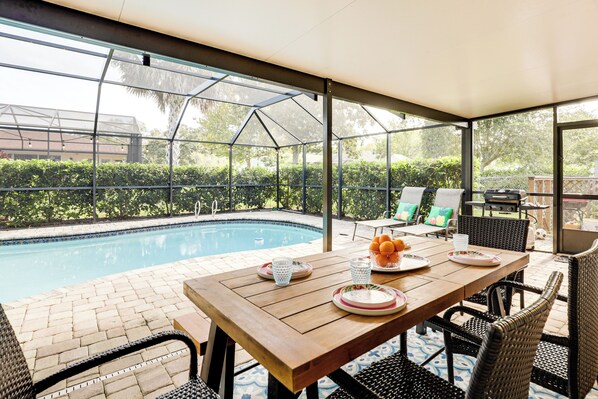 Un patio techado con piscina, mesa de madera, sillas de mimbre y vistas al jardín trasero.