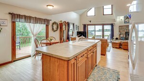 A spacious kitchen with a large island, wooden cabinets, and a view of a lake through the sliding glass doors. - Garage Game Room, Bar: Coldwater Lake House! (Coldwater)