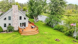 A house with a stone chimney, a deck with outdoor furniture, and a view of a lake. - Garage Game Room, Bar: Coldwater Lake House! (Coldwater)