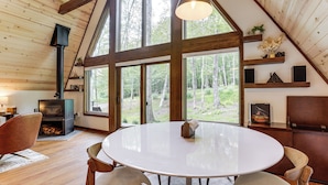 A spacious room with a large round table, wooden chairs, a fireplace, and large windows offering a view of the forest. - 1 Mi to Resort Beach: Alpine Lake A-Frame! (Terra Alta)