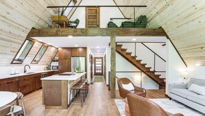 A spacious loft-style interior with a kitchen, dining area, and living room. A staircase connects the two levels. - 1 Mi to Resort Beach: Alpine Lake A-Frame! (Terra Alta)