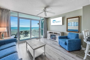 A spacious living area with a balcony, a ceiling fan, a TV, and a framed artwork.