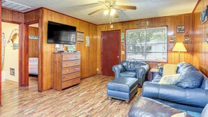 A room with a wooden floor, a ceiling fan, a television, a leather sofa, and a wooden dresser. - Shared Dock & Yard: Greers Ferry Lake Home! (Greers Ferry)