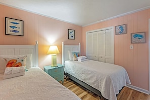Een slaapkamer met twee bedden, een nachtkastje met een lamp en een raam met luiken.