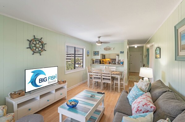 A living room with a television, a dining area with a table and chairs, and a kitchen in the background.