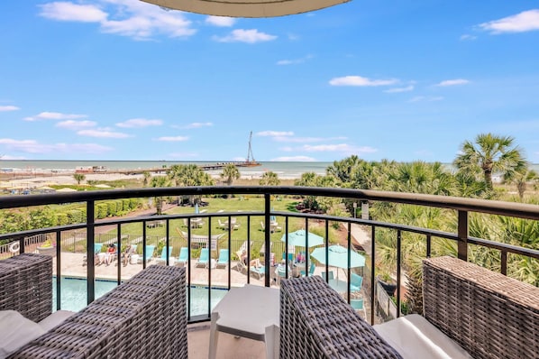 A balcony with wicker furniture, a pool, and a view of the beach and ocean.