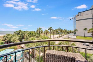 A balcony with a view of the beach, palm trees, and a building with a pool. - New Beautifully Remodeled, Meridian Plaza with Pools (Myrtle Beach)