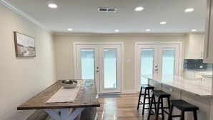 A modern kitchen with a wooden dining table, bar stools, and a large window. - Countryside Retreat - Come Relax, Unwind & Cast a Line (LaRue)