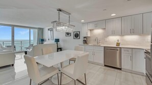 A modern kitchen with white cabinetry, a stainless steel dishwasher, and a dining area with a white table and chairs.