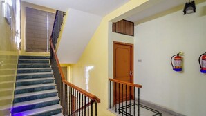 Un escalier avec une rampe en bois, un extincteur fixé au mur et une porte avec un cadre en bois.