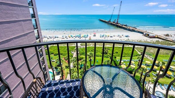 A balcony with a clear view of a beach, a pier, and a golf course.