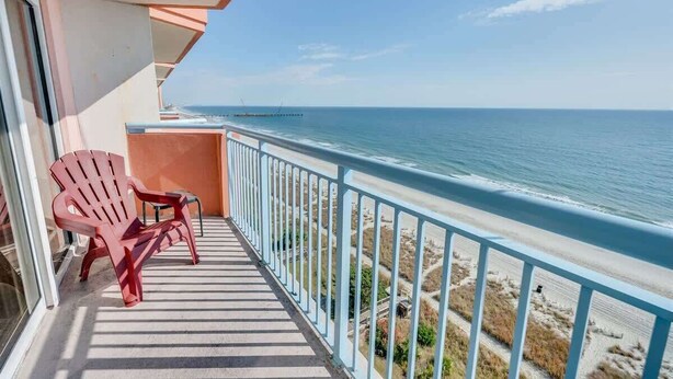 A balcony with a view of the ocean, a red chair, and a small table.