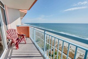A balcony with a view of the ocean, a red chair, and a small table.