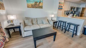 A living room with a sofa, a coffee table, and a kitchen area with a bar counter and stools.