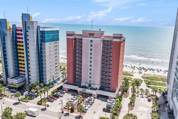 A multi-story hotel with a parking lot and a view of the beach.