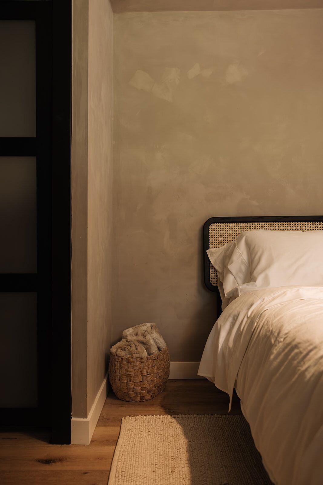 Ein Schlafzimmer mit Holzboden, einem gewebten Korb und einem Bett mit weißer Bettwäsche.