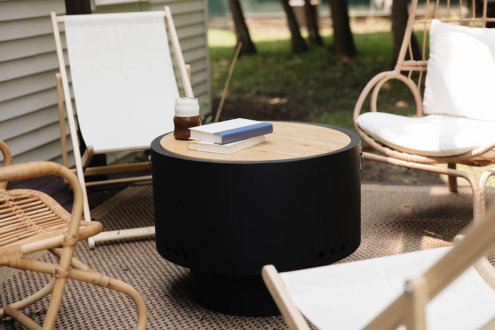 Een ronde zwarte tafel met een boek en een fles erop, omringd door rieten stoelen en een whiteboard.