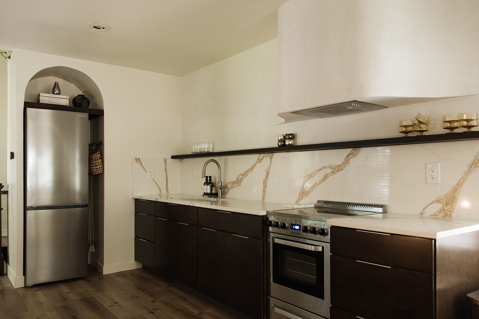 A modern kitchen with a stainless steel refrigerator, a built-in oven, and a marble backsplash.