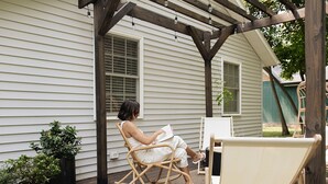 Una persona sentada en una silla de mimbre bajo una pérgola de madera, leyendo un libro.