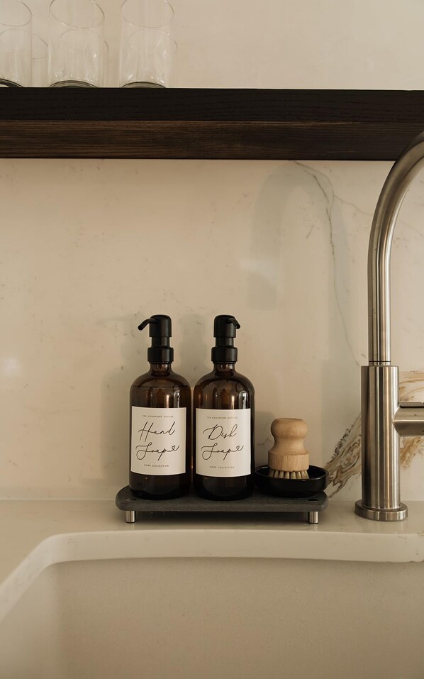Dos botellas de jabón para manos y platos sobre un estante encima de un lavabo con un cepillo de madera.