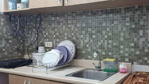 Une cuisine avec un mur recouvert de carreaux, un égouttoir à vaisselle, un évier et un plan de travail sur lequel se trouvent divers objets.