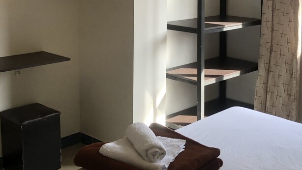 Une chambre d’hôtel avec un lit, un téléviseur fixé au mur, un meuble noir et une étagère intégrée.