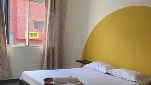 Une chambre d’hôtel avec un lit, une fenêtre avec des rideaux, un mur d’accent jaune et une vue sur un bâtiment rouge à l’extérieur.
