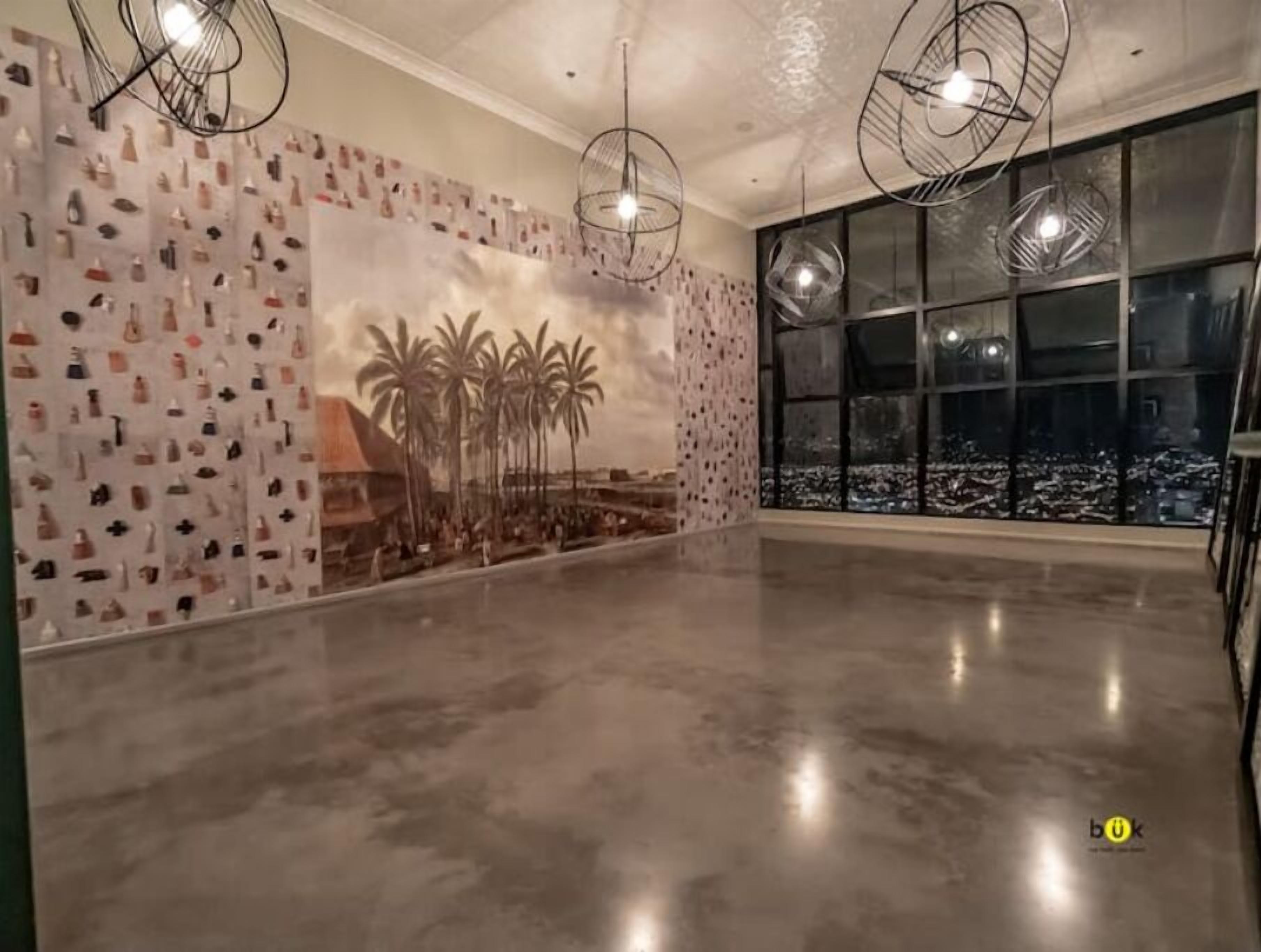 A spacious room with a polished concrete floor, a large window with a city view, and a wall decorated with various items and palm trees.