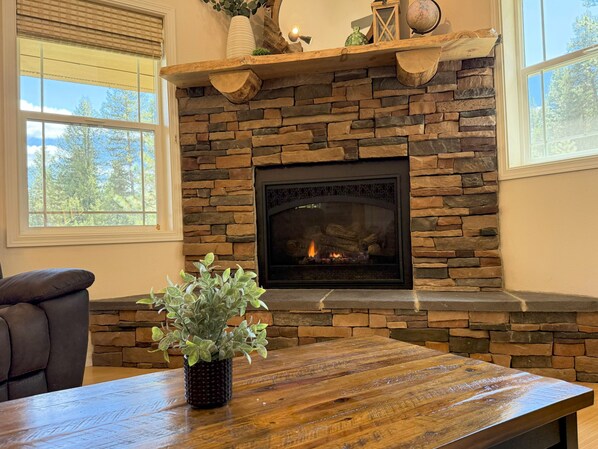 A stone fireplace with a fire, a wooden table with a plant, and a leather chair.