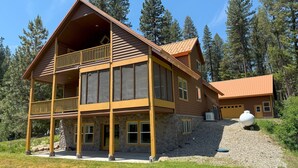 Une cabane en rondins à deux étages, dotée d’un balcon, de fondations en pierre et d’une cheminée en pierre.