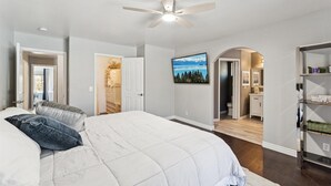 Une chambre à coucher avec un lit, un ventilateur de plafond, une armoire et une salle de bain visible à travers une arche.