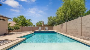 Une piscine rectangulaire à l’eau d’un bleu limpide, entourée d’un mur de briques et d’une terrasse en bois. On y trouve deux chaises longues et un parasol.
