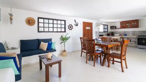 A living room with a sofa, coffee table, dining table with chairs, a kitchen area with cabinets and appliances, and a large window with a view. - LAMAU-Beachfront House, San Crisanto, Yuc. (San Crisanto)