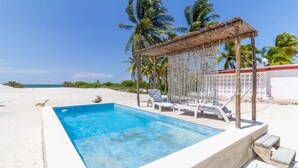 A rectangular swimming pool with a wooden pergola and lounge chairs on a sandy beach, surrounded by palm trees and a clear blue sky. - LAMAU-Beachfront House, San Crisanto, Yuc. (San Crisanto)