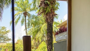 Un patio con suelo de piedra y vistas a un jardín exuberante, con palmeras y plantas con flores.