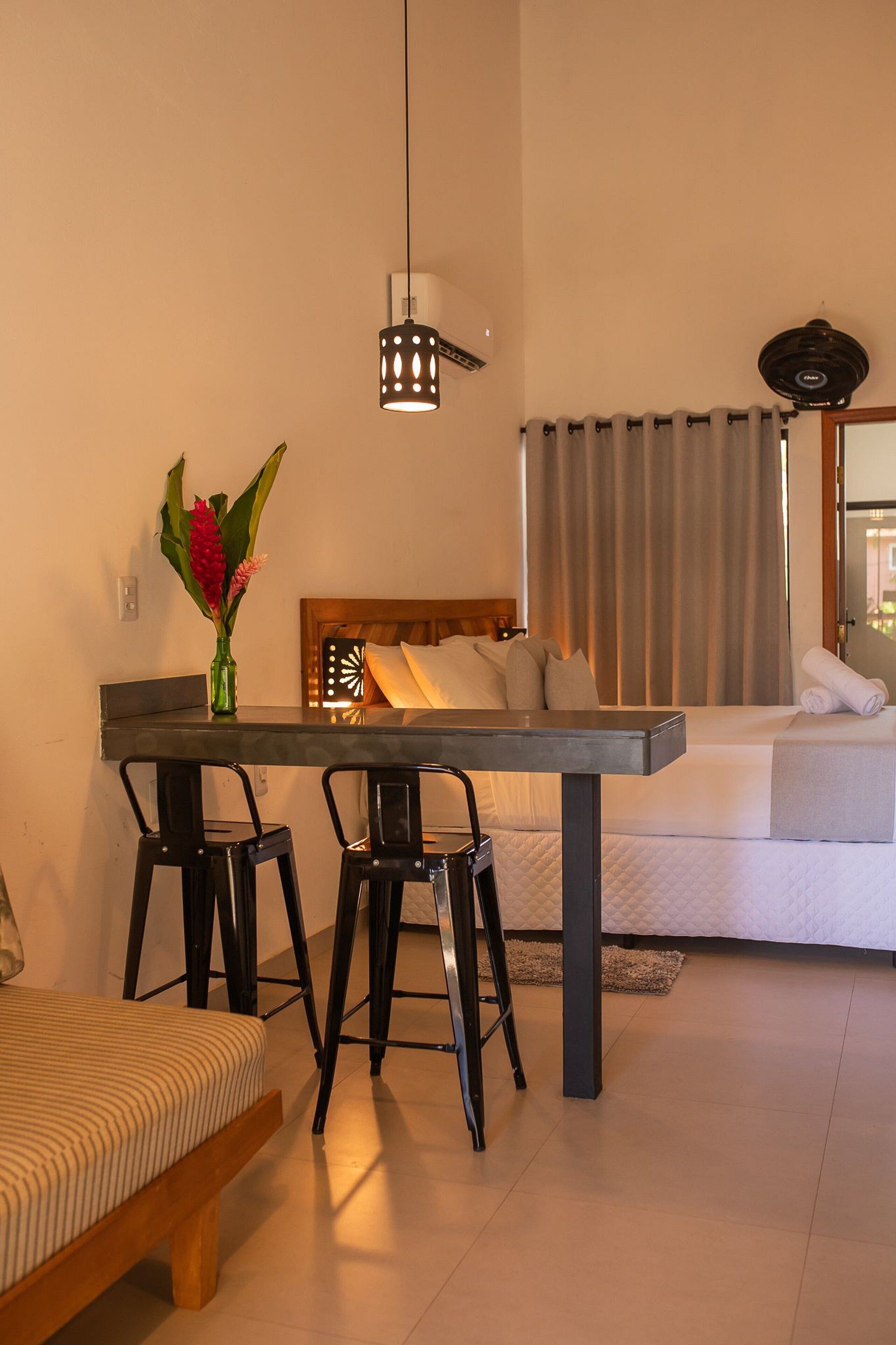 Una habitación de hotel moderna con comedor, cama y un amplio ventanal con cortinas.
