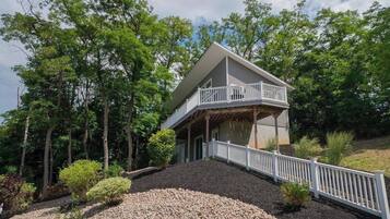 A two-story house with a balcony, surrounded by trees and a gravel driveway.