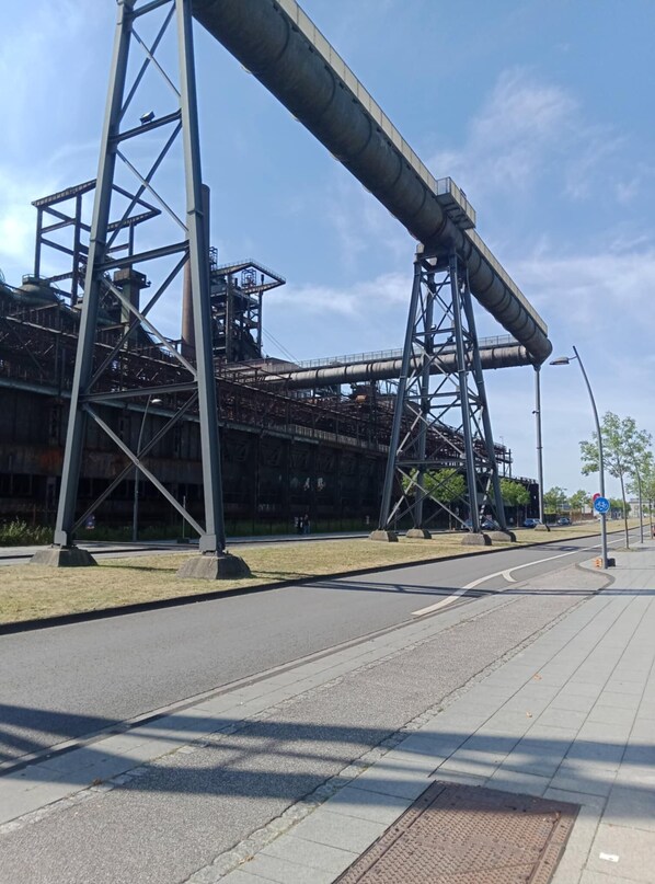 Une rue bordée d’un grand complexe industriel, comprenant une haute tour et un convoyeur.