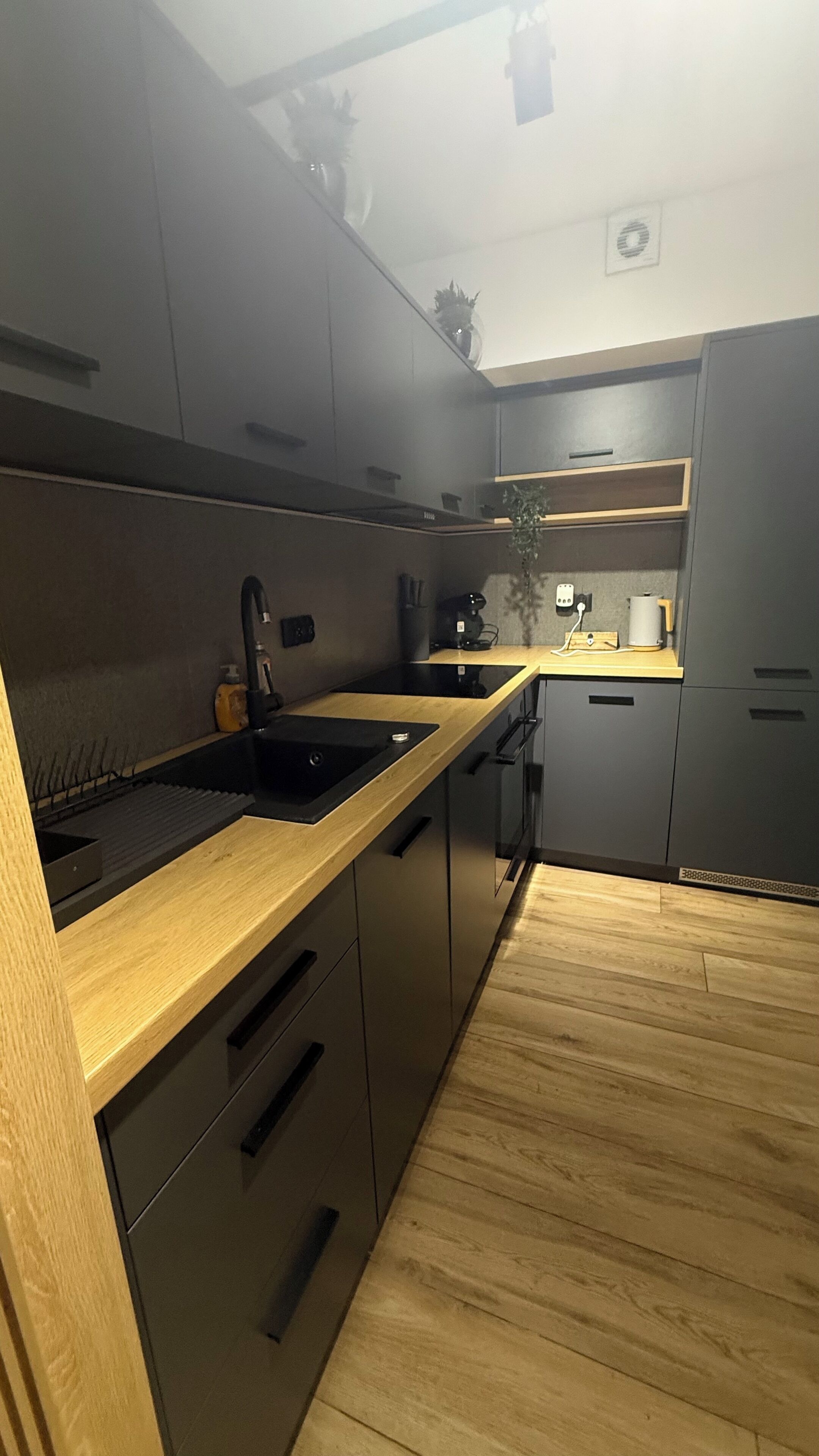 Een moderne keuken met donkere kastjes, een houten aanrechtblad en een geïntegreerde vaatwasser.