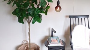 Een kamer met een potplant, een rieten mand, een stoel met een tijdschrift en een plank met boeken en decoratieve objecten.