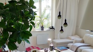 Een gezellige woonkamer met een witte bank, een bijzettafeltje en een grote groene plant.