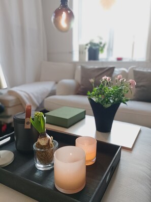 A cozy living room with a modern sofa, a small table with candles, a potted plant, and a speaker.