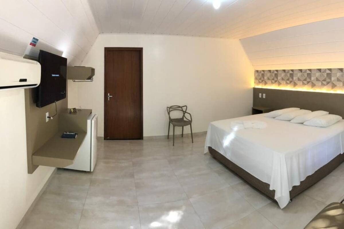 A bedroom with a bed, a desk, a chair, and a TV.