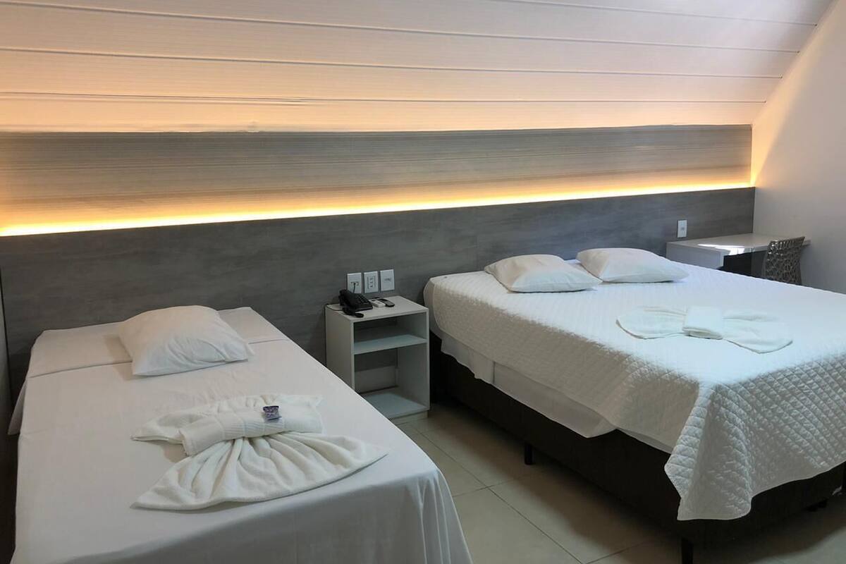 A hotel room with two beds, a nightstand, and a headboard with integrated lighting.