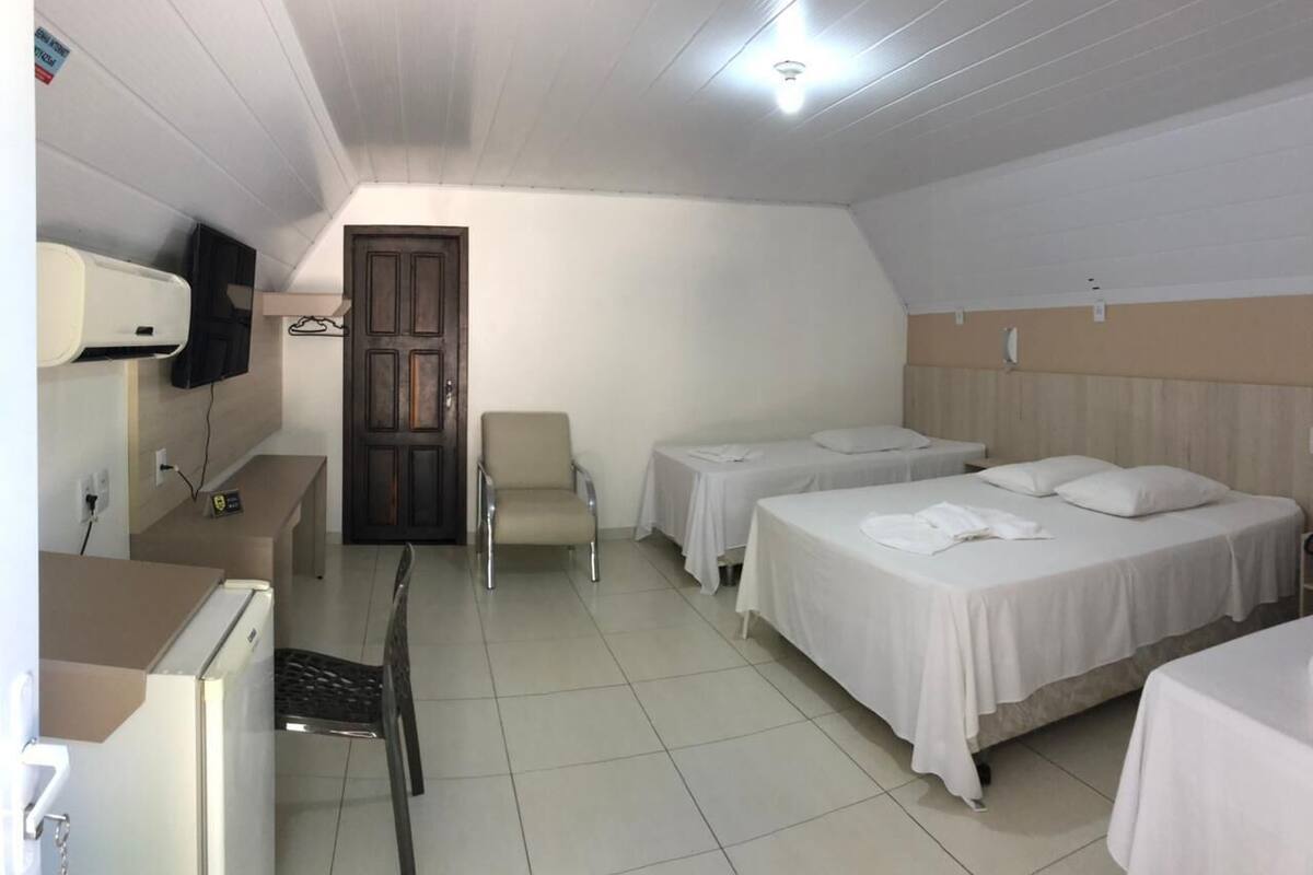 A hotel room with two beds, a desk, a chair, a TV mounted on the wall, and a door leading to another room.