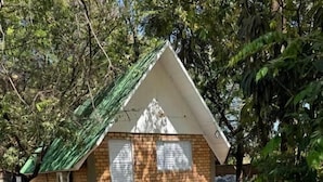 A small, triangular-roofed building with a brick exterior, a green bench, and a gravel ground. - HOTEL RECANTO DO BOSQUE (Sorriso)